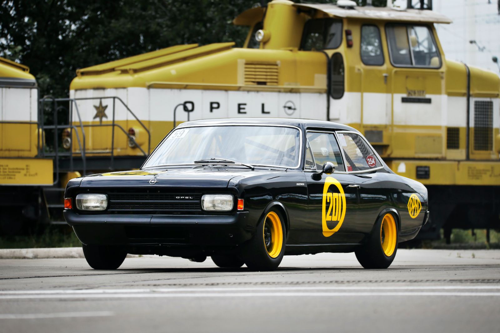 Schwarzer Opel vor gelben Rangierlokomotiven